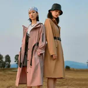 Zwei Frauen in langen Trenchcoats in Rosa und Khaki mit Gürtel auf einem Feld