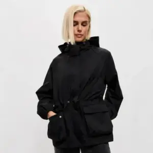 Frau in brauner Jacke mit Kordelzug und großen Taschen